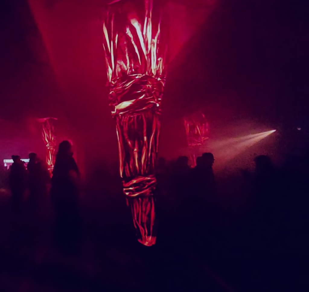 A red lit up object glows at Night Mass in Hobart's Dark Mofo 2026 festival. We see people dancing and a strange red glow in the background.
